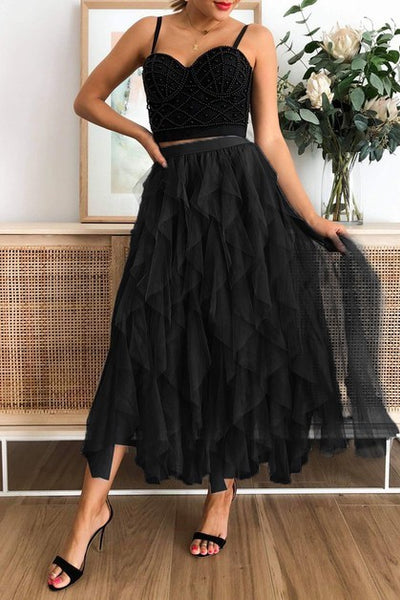 Woman wearing a black top with a black tulle skirt in a room with a vase and framed picture.