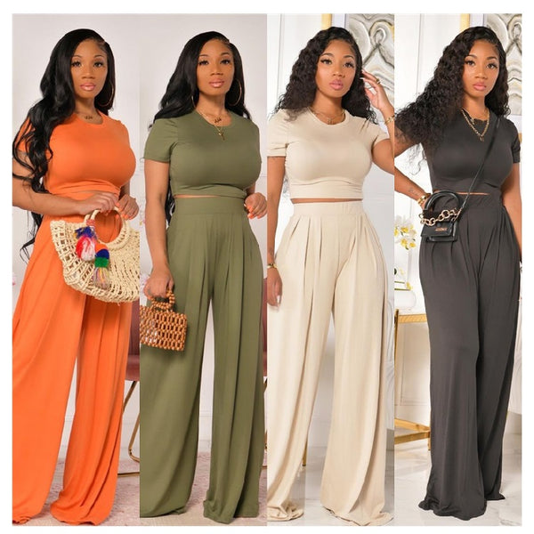 Four women wearing different colored pants with matching tops against a neutral background.