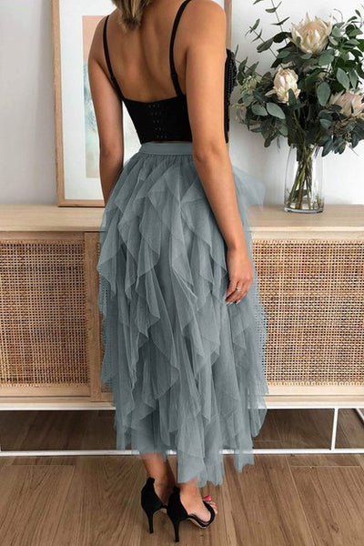 Person wearing a black top and gray tulle skirt in a room with a wooden cabinet and flowers.