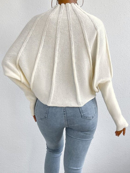Person wearing a white sweater and light blue jeans on a plain background