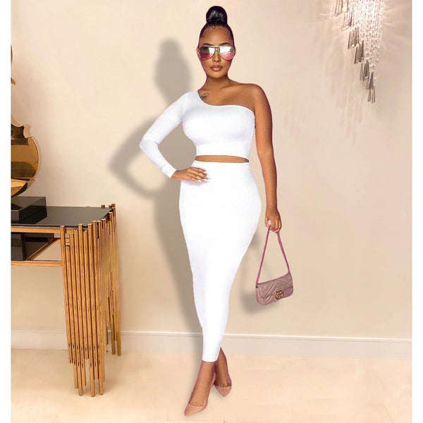 Woman in a white one-shoulder outfit holding a handbag indoors.