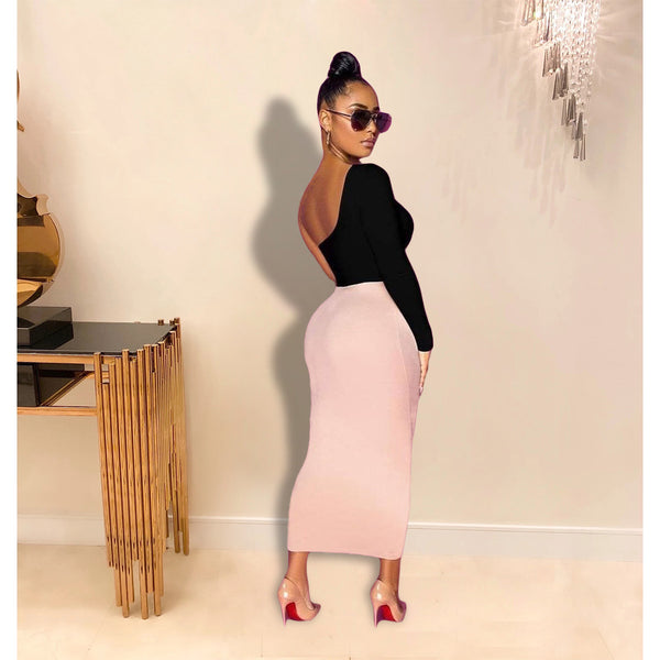 Woman in black top and pink skirt standing in a room with a decorative wall and table.