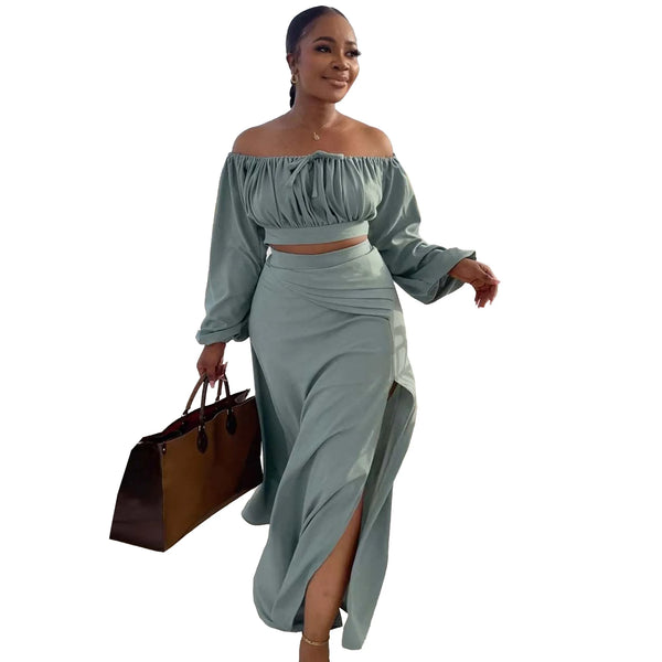 Woman wearing a light green off-shoulder top and skirt set, holding a brown handbag on a white background.
