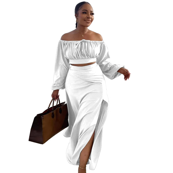 Woman wearing a white off-shoulder top and skirt set, holding a brown handbag on a white background.