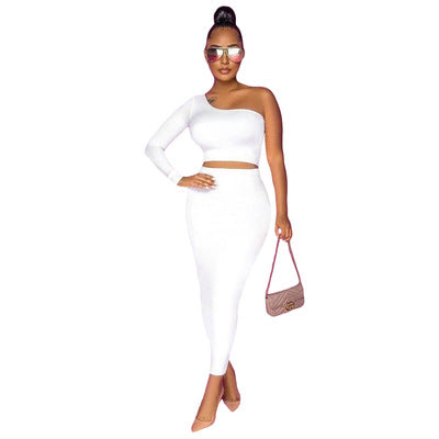 Woman wearing a white one-shoulder top and high-waisted skirt, holding a pink handbag on a white background.