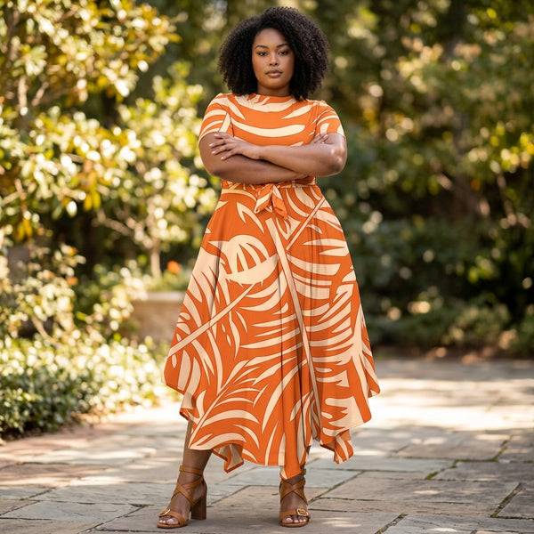 SlayEdgeBoutique model wearing an orange and cream tropical print short sleeve maxi dress with a tie waist in a garden.